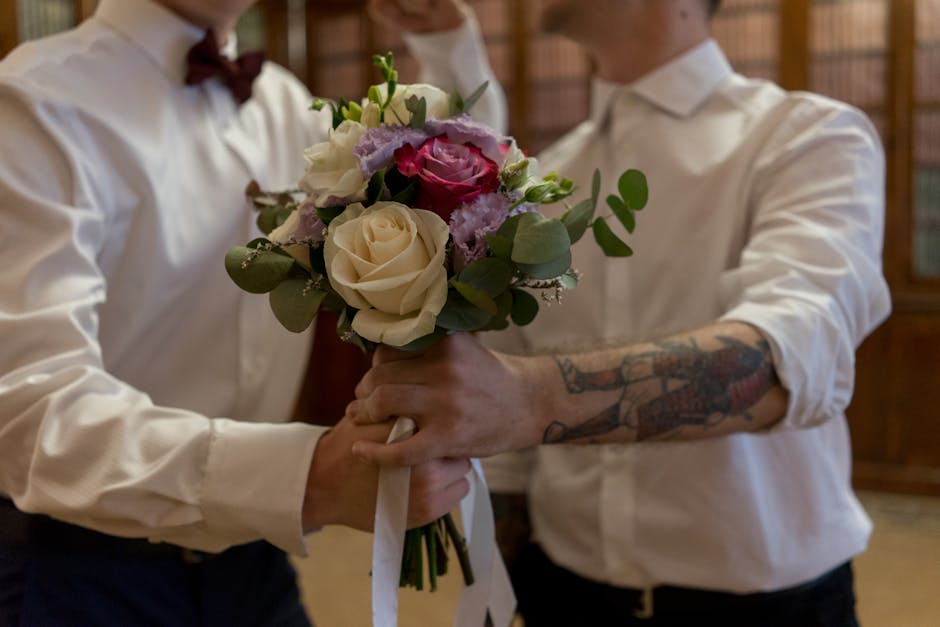 A floral arrangement featuring white and pink roses, purple lisianthus, and greenery being handed over in a bouquet, with the hands of two people visible — one holding the bouquet and the other rece